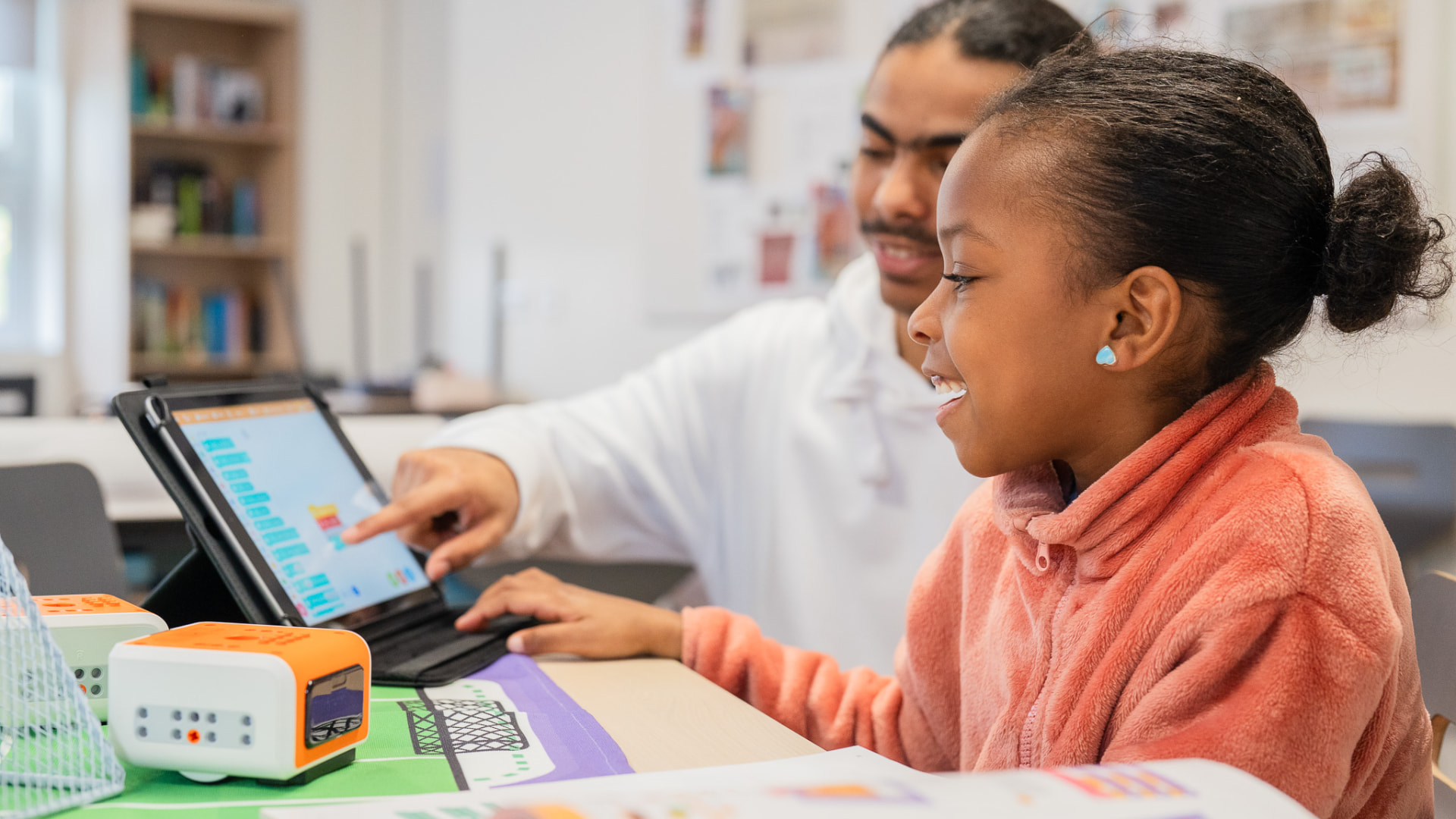 Begeleider van Ahamoto Club helpt een kind met programmeren op een tablet
